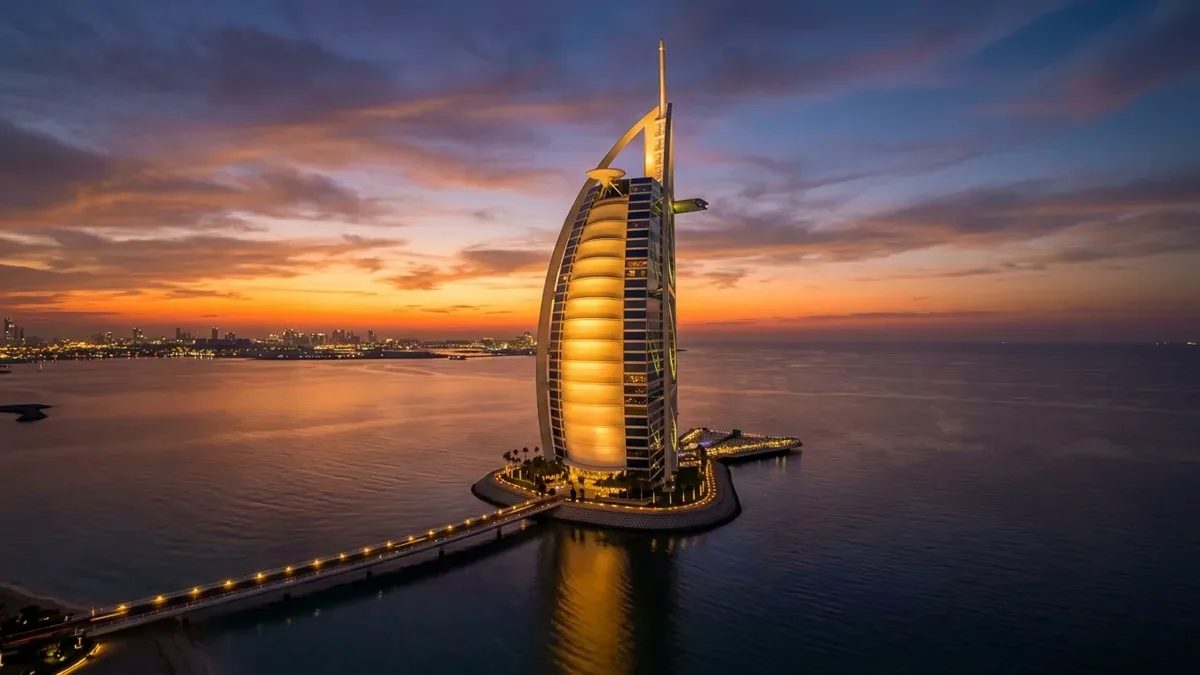 Edificio de hotel con forma de vela iluminado al atardecer frente al mar, sin personas