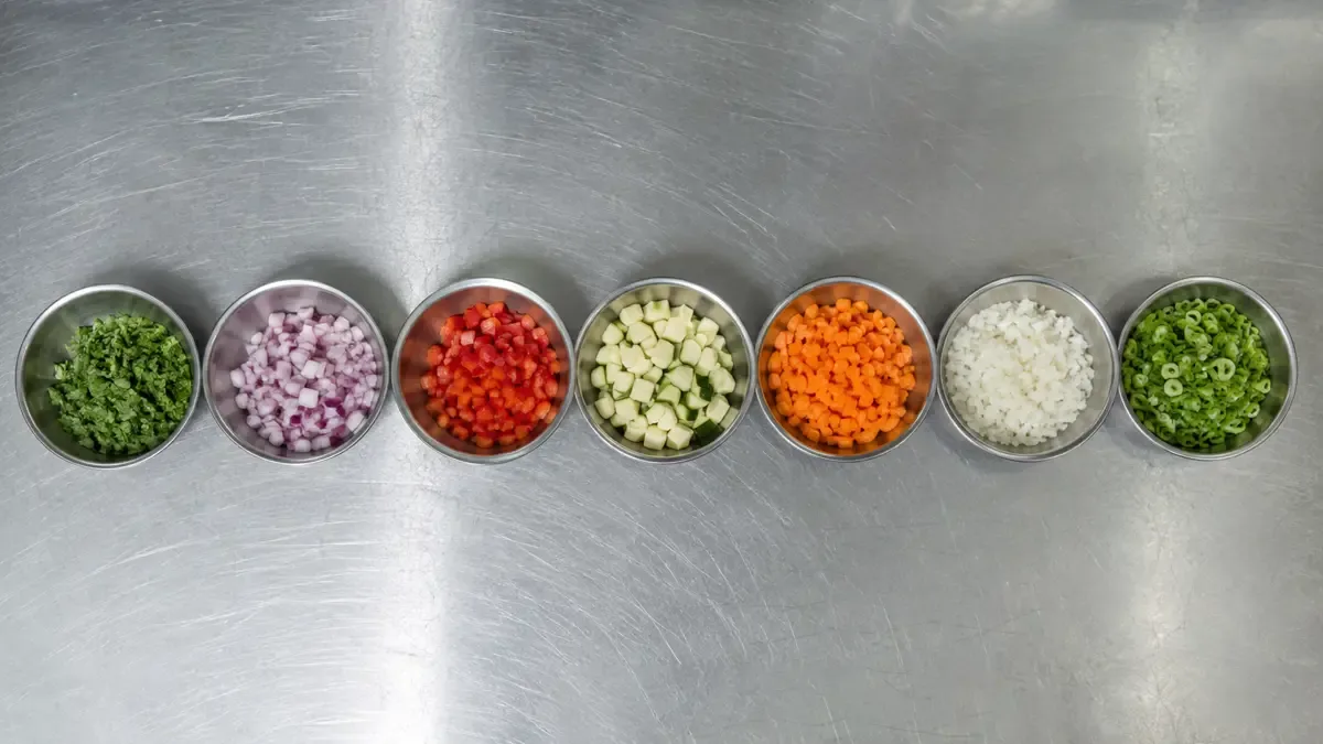 Hilera de bowls metálicos con ingredientes picados sobre una mesada