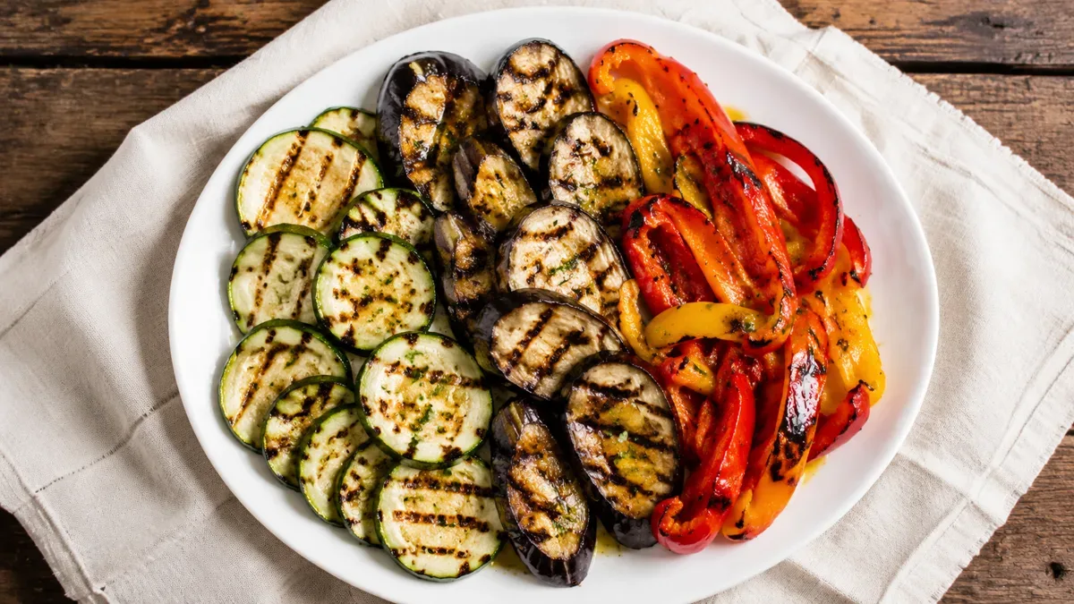 Verduras variadas a la plancha con marcas doradas, servidas en un plato de loza sobre mesa de madera